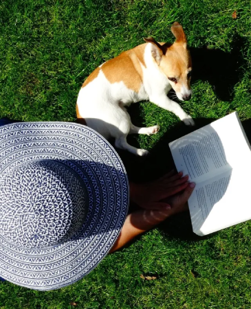 A person sitting in the grass with a dog and book.